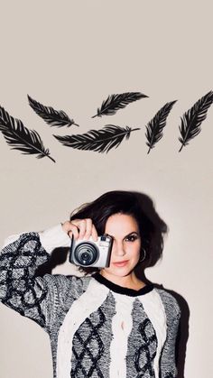 a woman holding a camera in front of a wall with black feathers flying above her