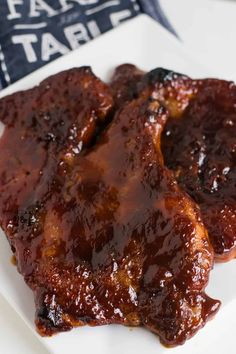 two pieces of meat covered in bbq sauce on a white plate