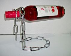 a red wine bottle is chained to a metal chain on a white counter top with a glass of wine in the background