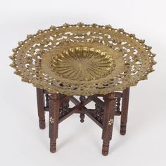 an ornately designed brass tray sits on top of a wooden stand with two legs