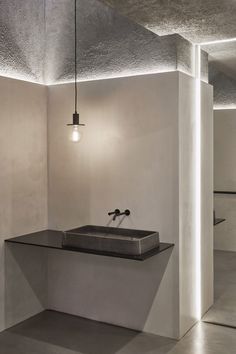 an empty bathroom with concrete walls and flooring is lit by light bulbs hanging from the ceiling