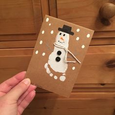 a hand holding up a brown card with a snowman on it