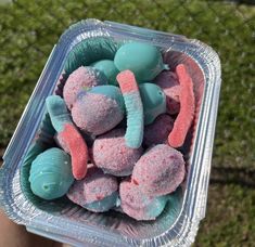 a plastic container filled with candy covered in blue and pink sprinkles on top of green grass