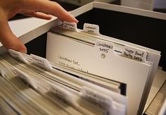 a person's hand reaching for several files in a file cabinet with labels on them