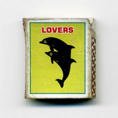 a matchbox with a dolphin on it and the words lovers written in red letters