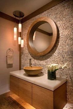 a bathroom sink under a round mirror next to a vase with flowers