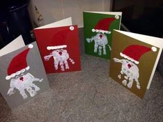 three christmas cards with handprints and santa hats on them, sitting on a counter