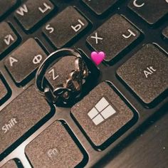 a pink heart sitting on top of a computer keyboard next to a keychain