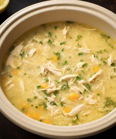 a white bowl filled with soup next to a slice of lemon on top of a table