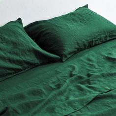 a bed with green sheets and pillows on top of it, against a white wall