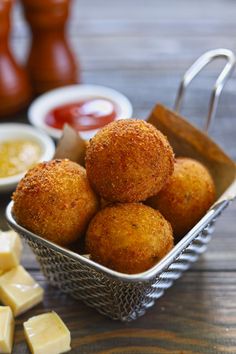 some food is in a metal basket on a table with sauces and cheese cubes