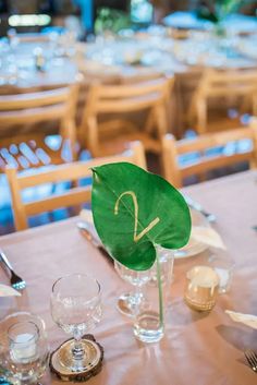 the table is set with glasses, silverware and a green leaf on top of it