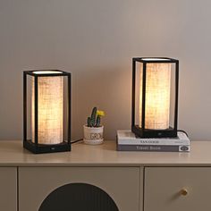 two lamps sitting on top of a table next to a book and plant in a vase