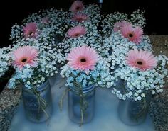 pink and white flowers are in mason jars on a counter top, with baby's breath