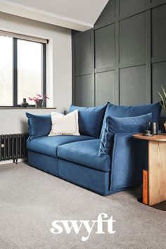 a blue couch sitting in front of a window next to a table and radiator