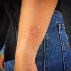 a person's arm with a small sunburst tattoo on the left forearm