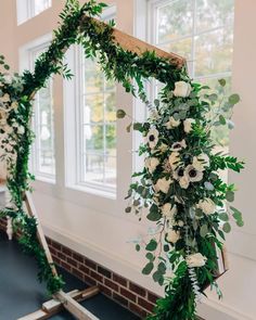 an arch with greenery and white flowers on the floor in front of a window