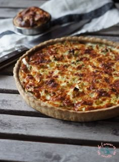 a pizza sitting on top of a wooden table next to a knife and fork with another pie in the background