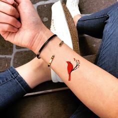 a woman's arm with a small red bird tattoo on the left side of her wrist