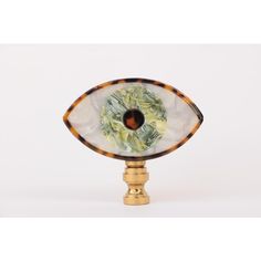 an eyeball shaped glass object on a gold plated base with leaves and flowers