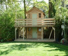 a small wooden house sitting in the middle of a lush green field next to trees