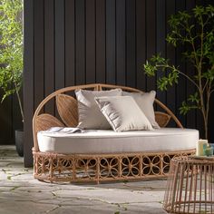 a wicker day bed with pillows on it in front of a black wall and potted plant