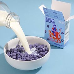 a person pouring milk into a bowl filled with blueberries next to a carton of milk