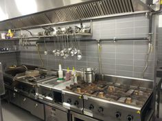 an industrial kitchen with pots and pans hanging from the ceiling, along with stainless steel appliances