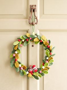 a wreath hanging on the front door of a house decorated with pom - poms and leaves