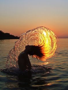 a woman is in the water with her hair blowing back and holding onto an object