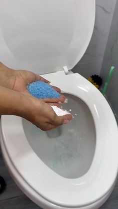 a person cleaning a toilet with a blue sponge