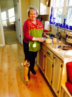 an older woman is standing in the kitchen with her dog