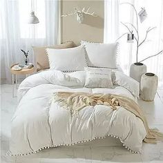 a bed with white comforters and pillows in a room next to a window,