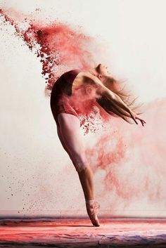 a ballerina in pink and white doing a dance move with colored powder behind her