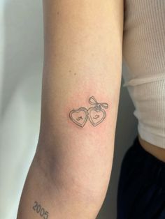 a woman's arm with two hearts and a bow tattoo on the left side of her arm