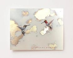 two birds flying in the air near each other on a piece of paper with gold foil