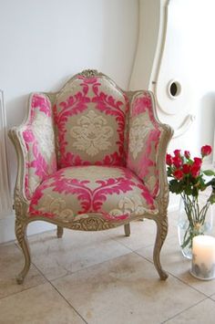 a pink and white chair sitting next to a vase with red flowers in front of a mirror