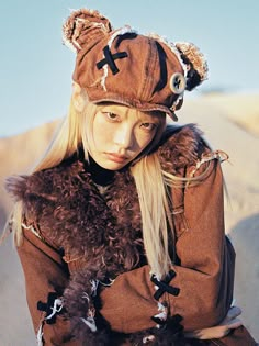 a woman with long blonde hair wearing a brown coat and hat while holding a teddy bear