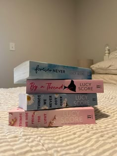 four books stacked on top of each other on a bed with white sheets and pillows