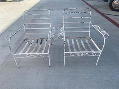 two white metal chairs sitting on top of a parking lot