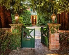 an entrance to a home with green gates and brick walkway leading into the front yard