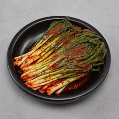 a black plate topped with asparagus covered in sauce and seasoning on top of it