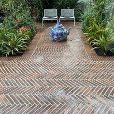 an outdoor patio with potted plants and two chairs in the back ground, surrounded by greenery