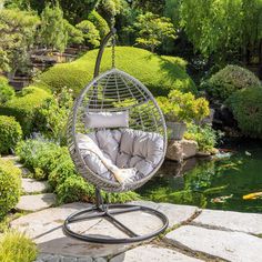 an outdoor swing chair in the middle of a garden with water and plants around it