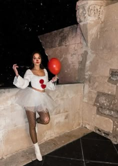 a woman in a white dress holding a red ballon and posing for the camera