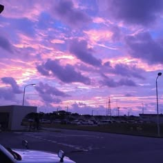 the sky is purple and pink as it sits in an empty parking lot with parked cars