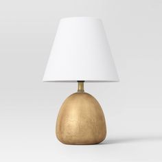 a gold table lamp with a white shade on the top and bottom part of it