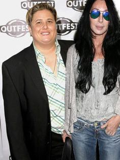 two women standing next to each other in front of a white wall with the words outfest written on it