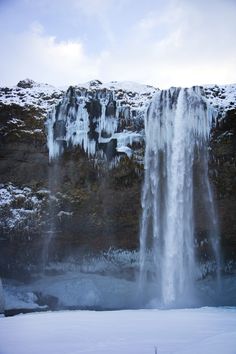 a large waterfall with snow on the ground and ice hanging off it's sides