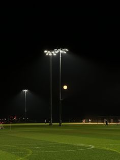 an empty soccer field at night with the lights on and people playing in the background